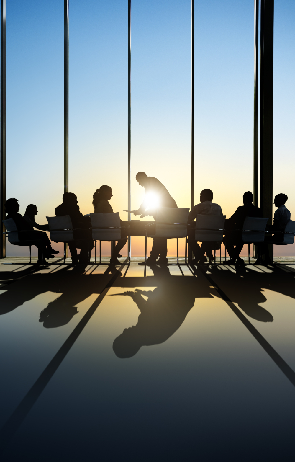 business people sitting around a table in a large empty room with big windows and a sunset