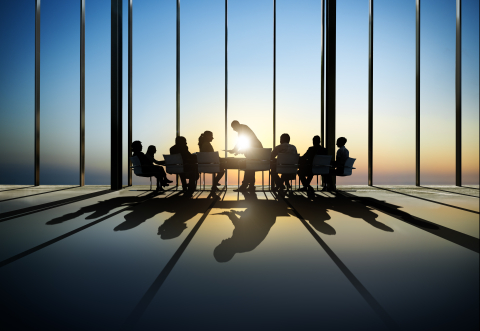 business people sitting around a table in a large empty room with big windows and a sunset